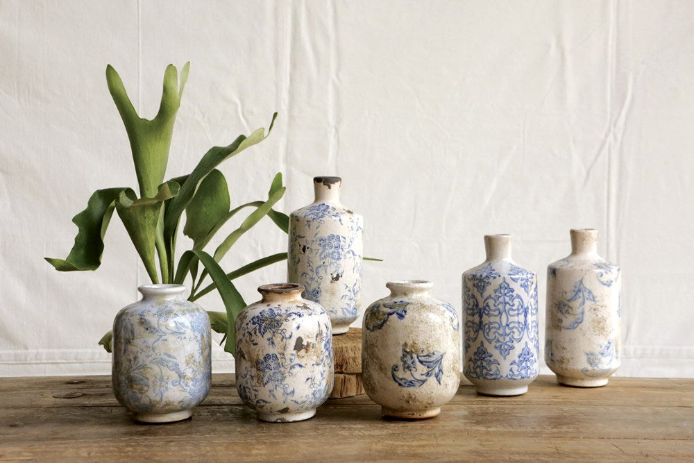 assorted styles and sizes of off-white and blue vases arranged together on a wooden shelf with a plant.