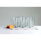 multiple recycled glass drinking glasses displayed next to sliced fruit on a placemat against a light gray wall