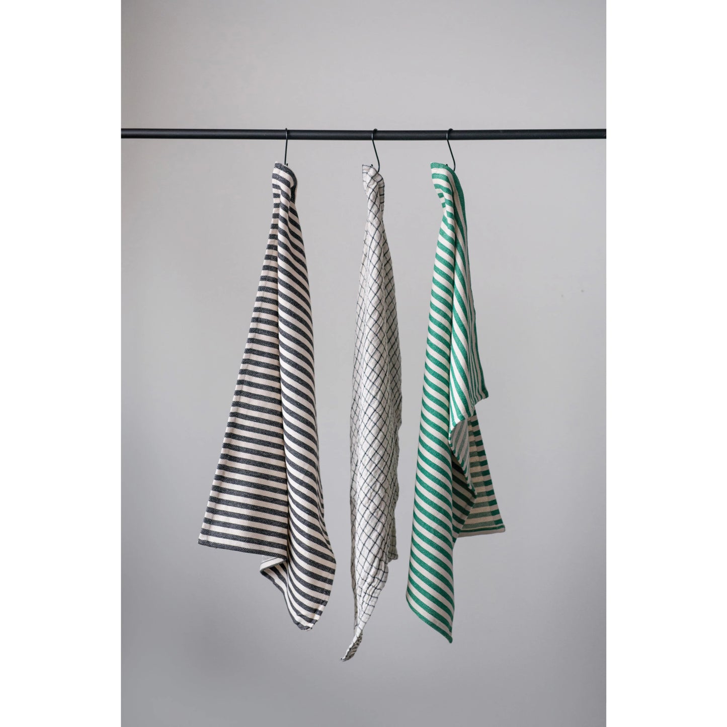 three different patterned cotton tea towels hanging against a light gray background