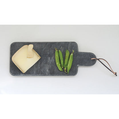 black marble cheese board displayed with slice of cheese and sugar snap peas on a light gray background