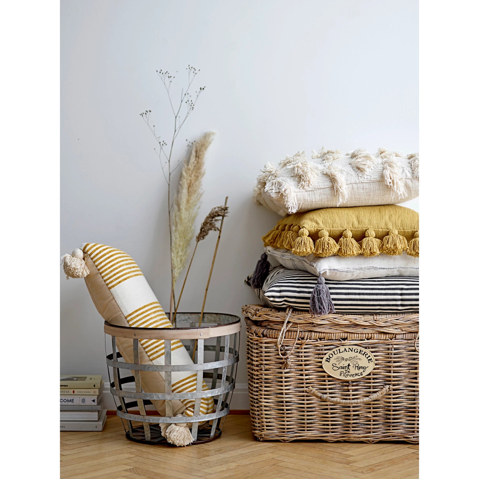 the black and white striped pillow displayed with multiple pillows stacked on a basket next to a metal basket filled with a pillow and decorative picks sitting on the wood floor 