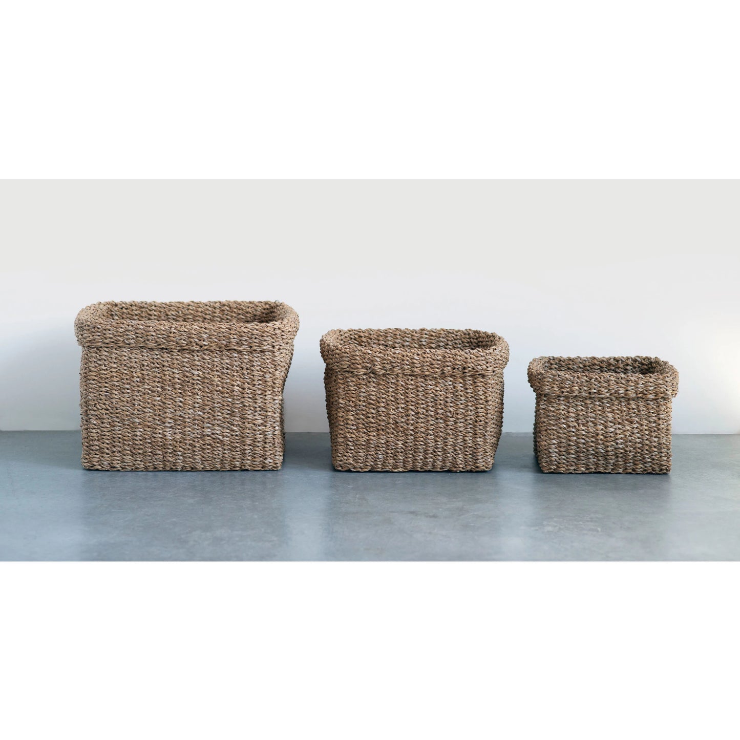 all three sizes of woven seagrass baskets displayed on a light gray surface against a white background