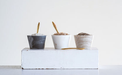 3 marble bowls filled with spices, 1 each of grey, white, and neutral each with a gold spoon.