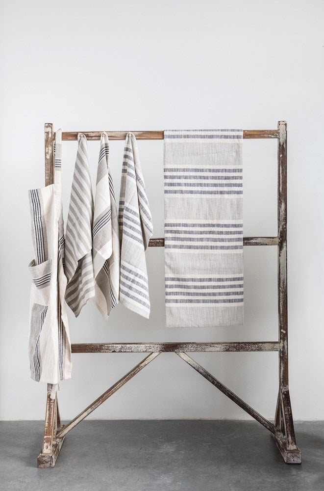 multiple woven cotton striped tea towel hanging on a distressed wooden rack against a white wall