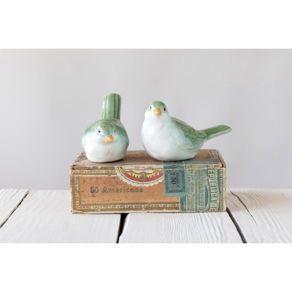 2 ceramic birds set on a decorative box on a wooden table.