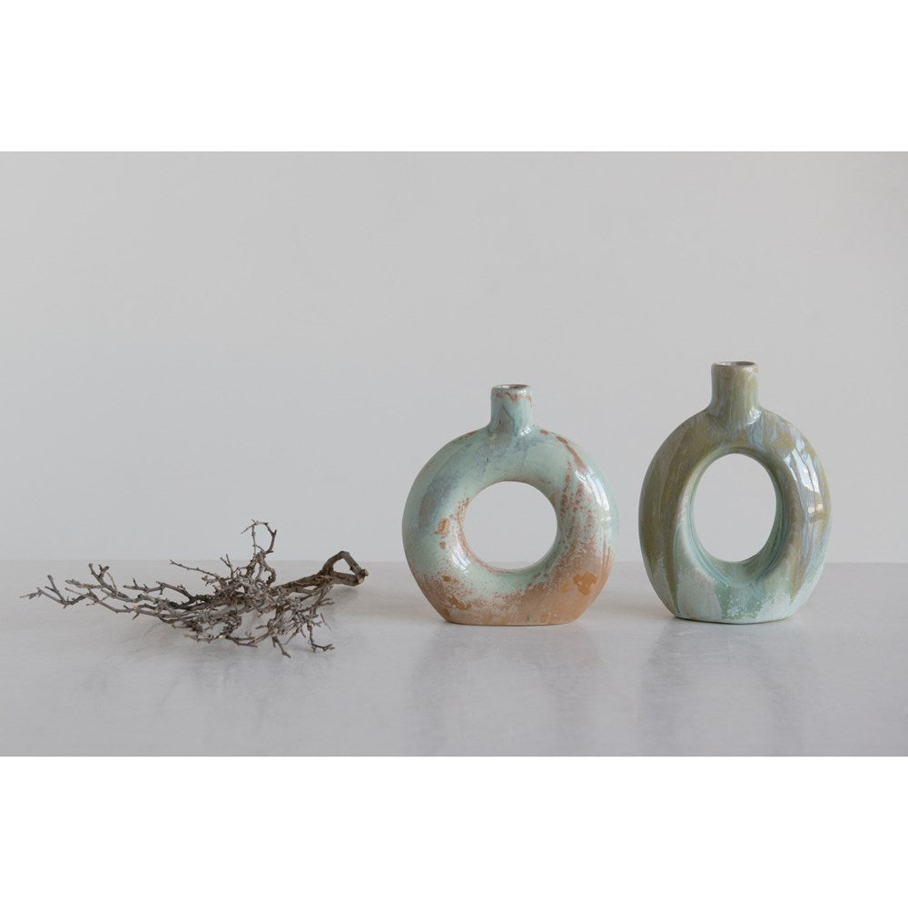 both oval and round stoneware cutout vases displayed next to twigs on a light gray surface