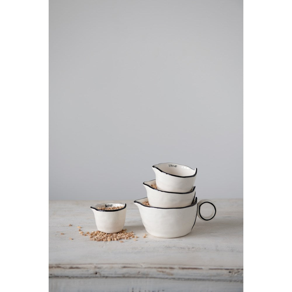 3 black and white measuring cups stacked with the forth and smallest one set next to them, all filled with grains.