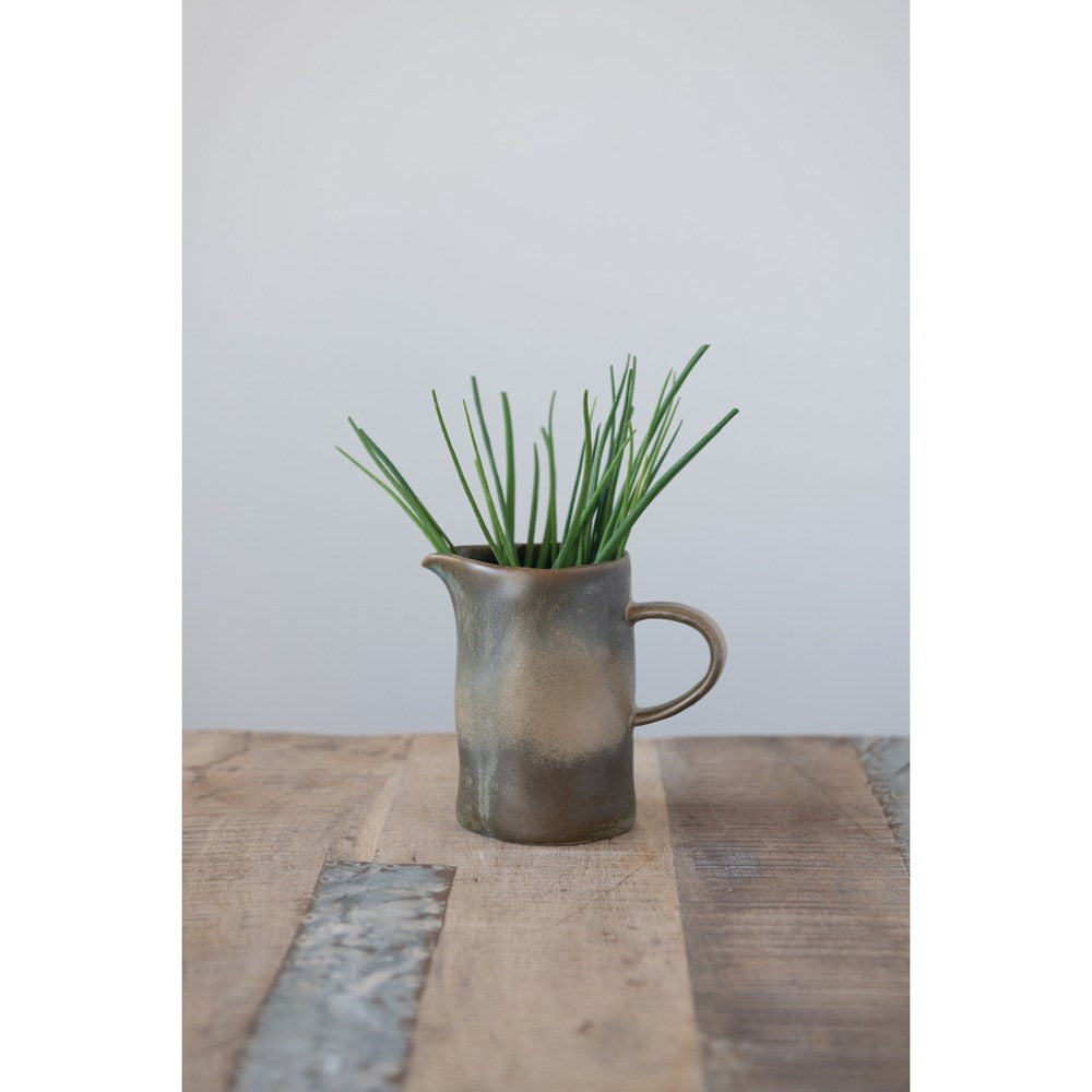 stoneware creamer with reactive glaze displayed on a reclaimed wood table with greenery inside against a gray background