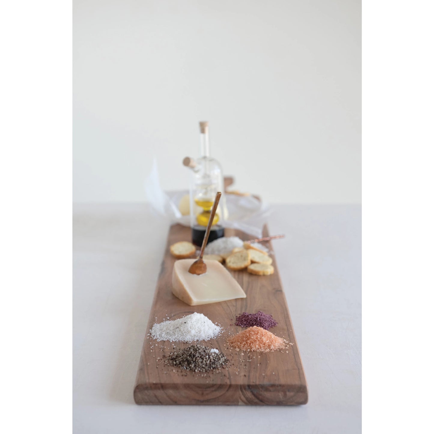 acacia oversized entertaining board displayed lengthwise with spices cheese crackers and oils on a white background