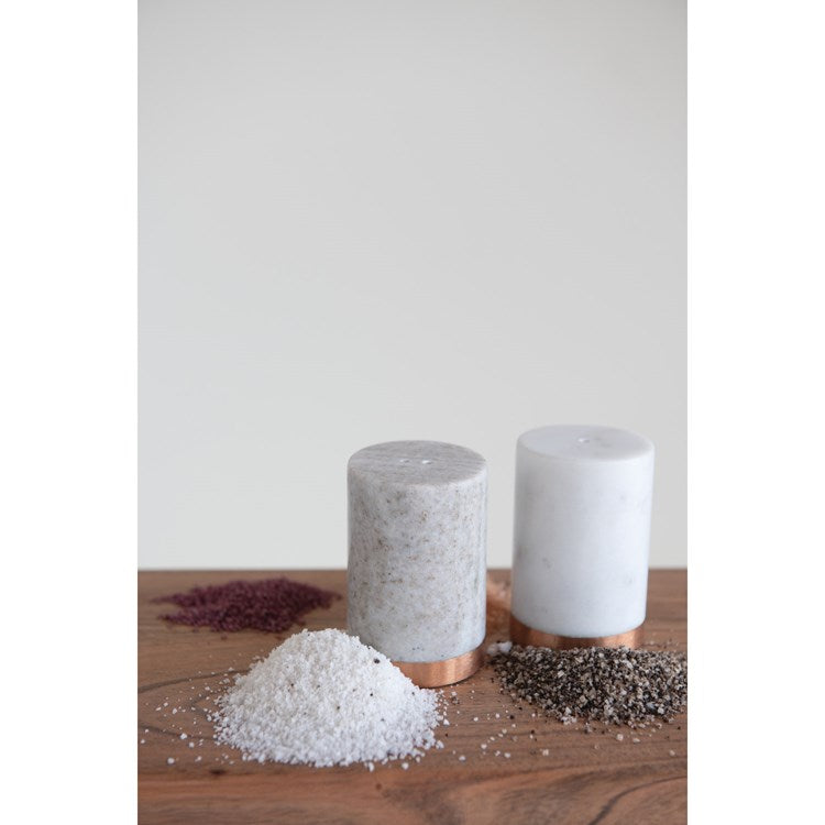 marble salt and pepper shaker set displayed on a dark wood surface with a small salt pile, pepper pile, and cayenne pepper 