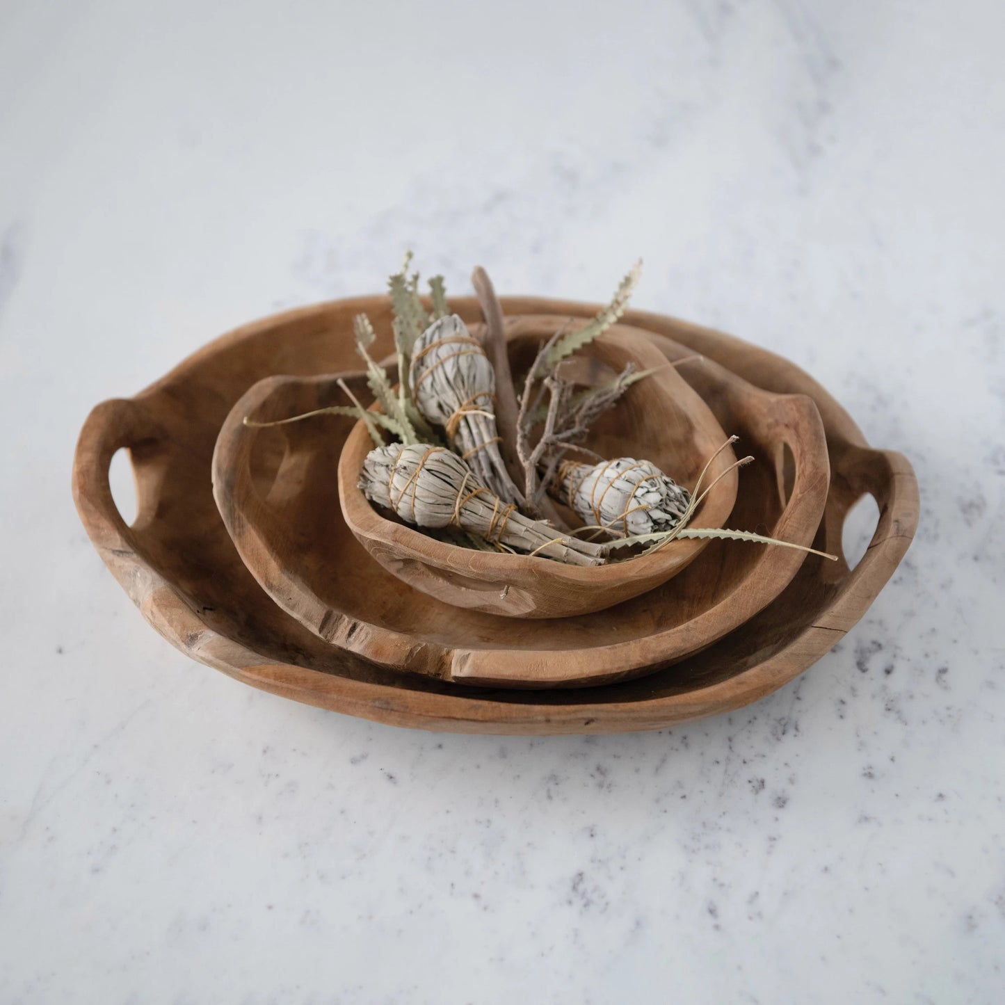 all three sizes of teak wood bowls with handles stacked on a light marble surface with dried bulb inside