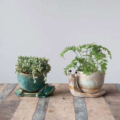side view of the stoneware planter with frog base filled with succulents and displayed on a rustic wooden surface next to another potted plant
