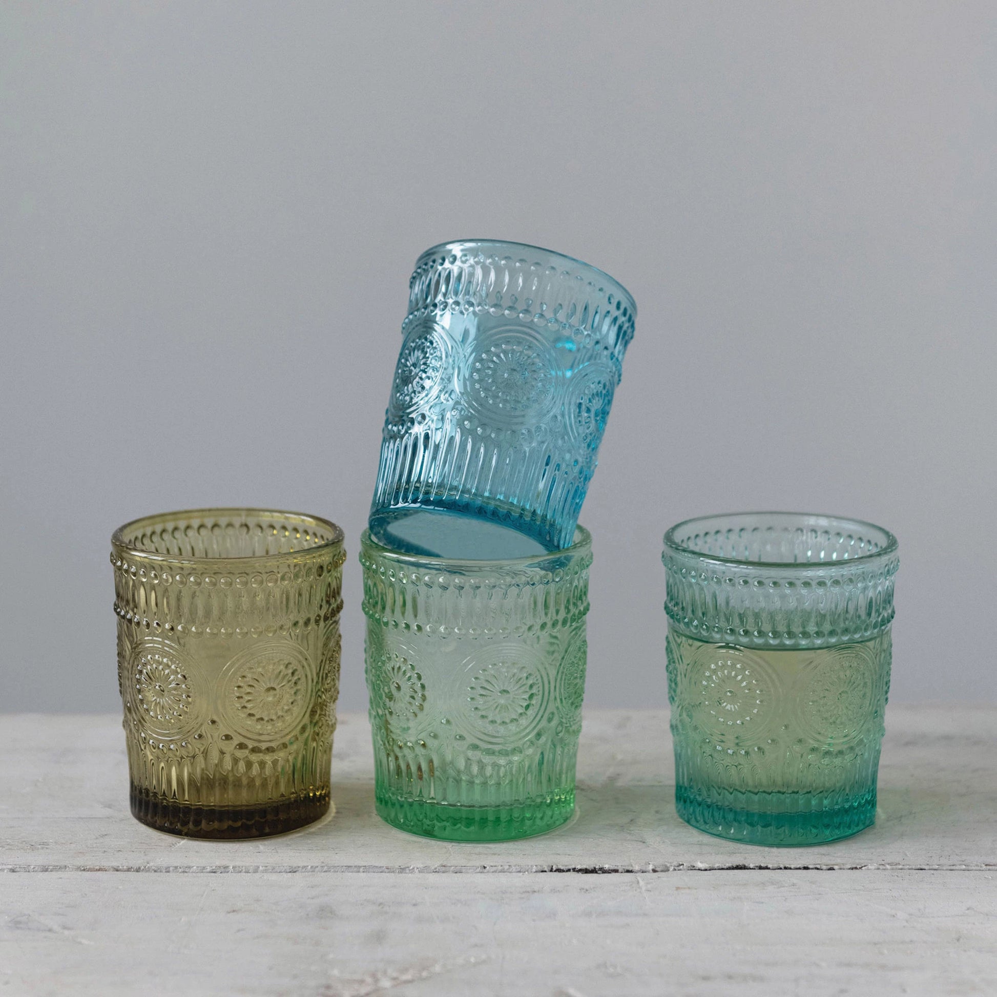 4 drinking glasses with embossed patterns on a wooden table, one glass is stacked on top of another.
