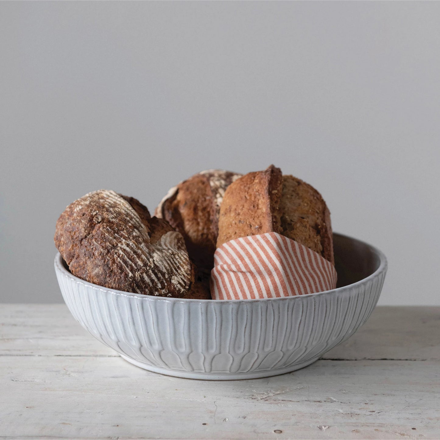 debossed stoneware bowl displayed with loaves bread inside on a white wooden table against a light gray background