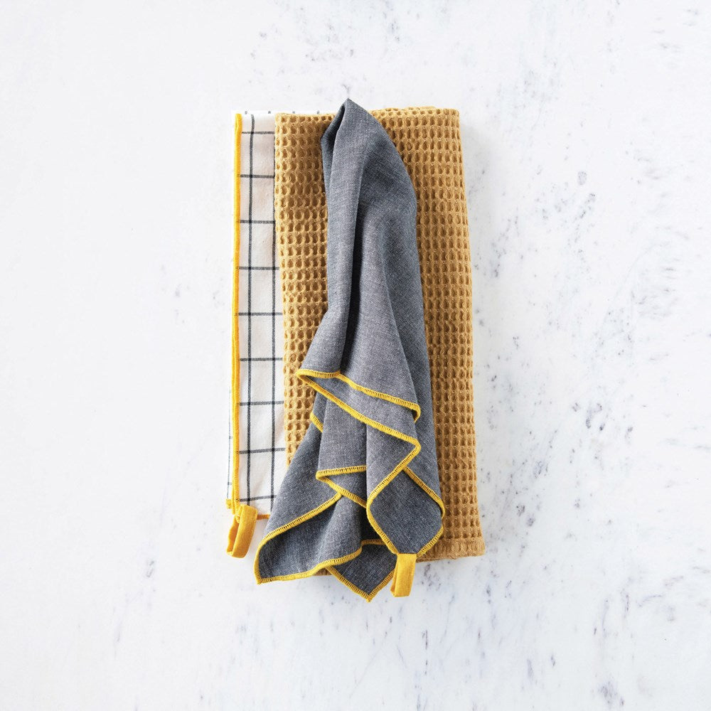 all three cotton tea towels displayed folded and stacked on a white marble surface