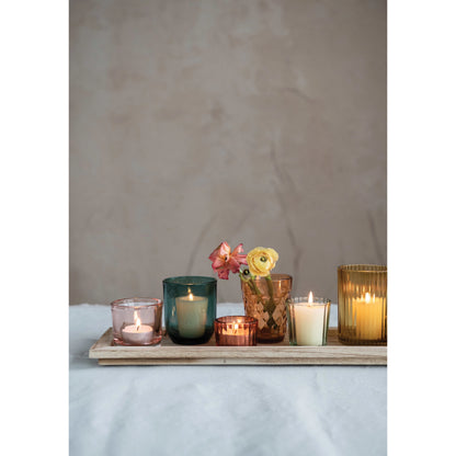 close up view of embossed glass votive holders filled with votives and flowers sitting on the wooden tray on a soft white table runner