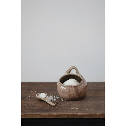 stoneware pot with spoon displayed on a rustic wood table against a light gray background