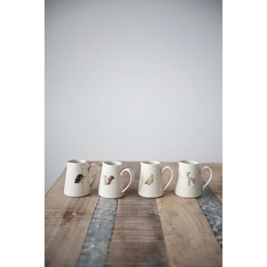 four different styles of creamer with forest animals on a rustic wooden table against a white background