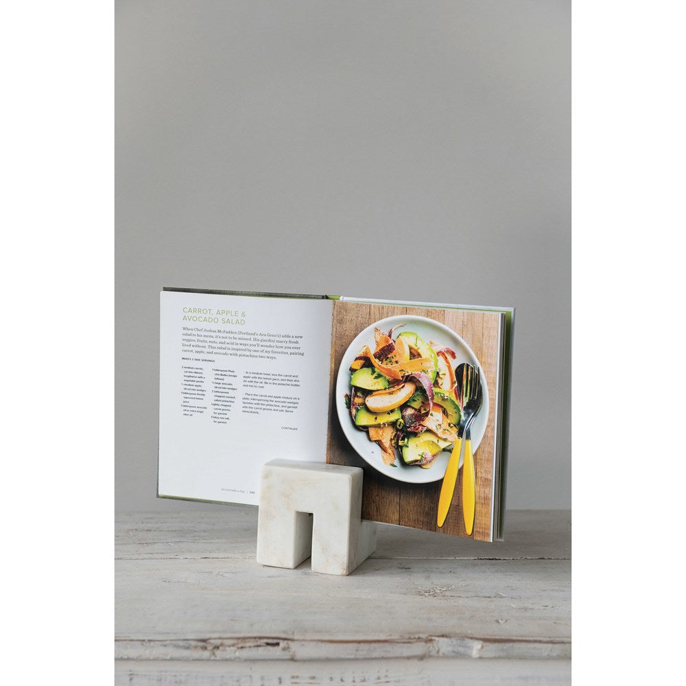 marble cookbook stand holding a cookbook on a white wood table against a gray background