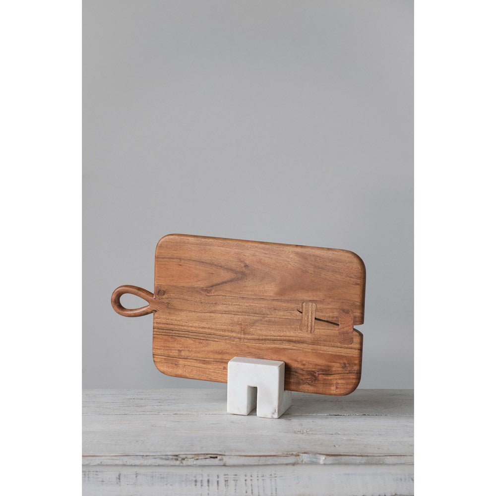 marble cookbook stand holding a wood cutting board on a white wood table against a gray background