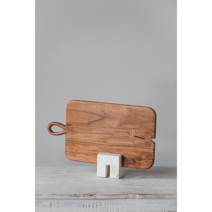 marble cookbook stand holding a wood cutting board on a white wood table against a gray background