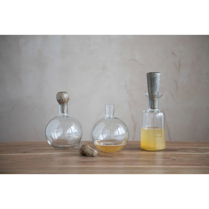 two glass decanters with mango wood stopper displayed next to a jug with funnel on a wooden surface against a gray background