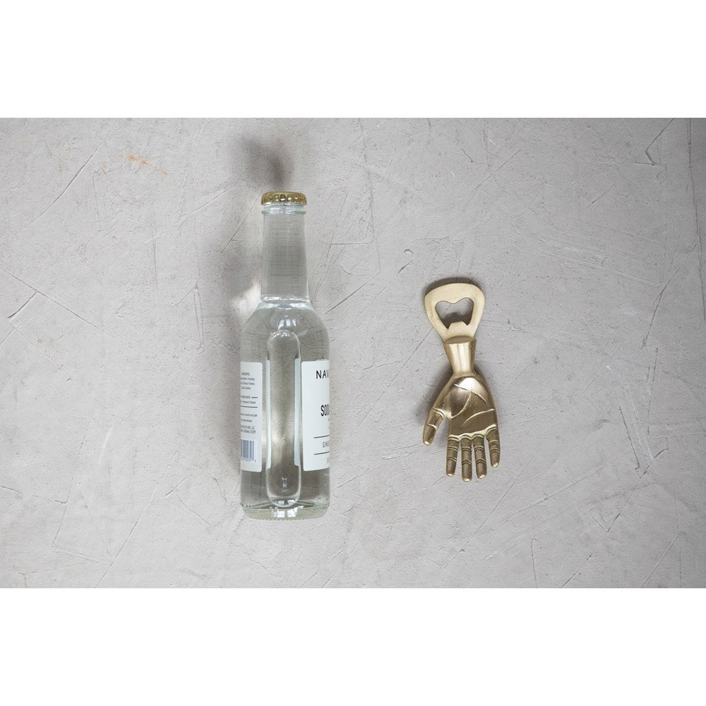 brass hand bottle opener displayed on a light gray surface next to a bottle on a white background