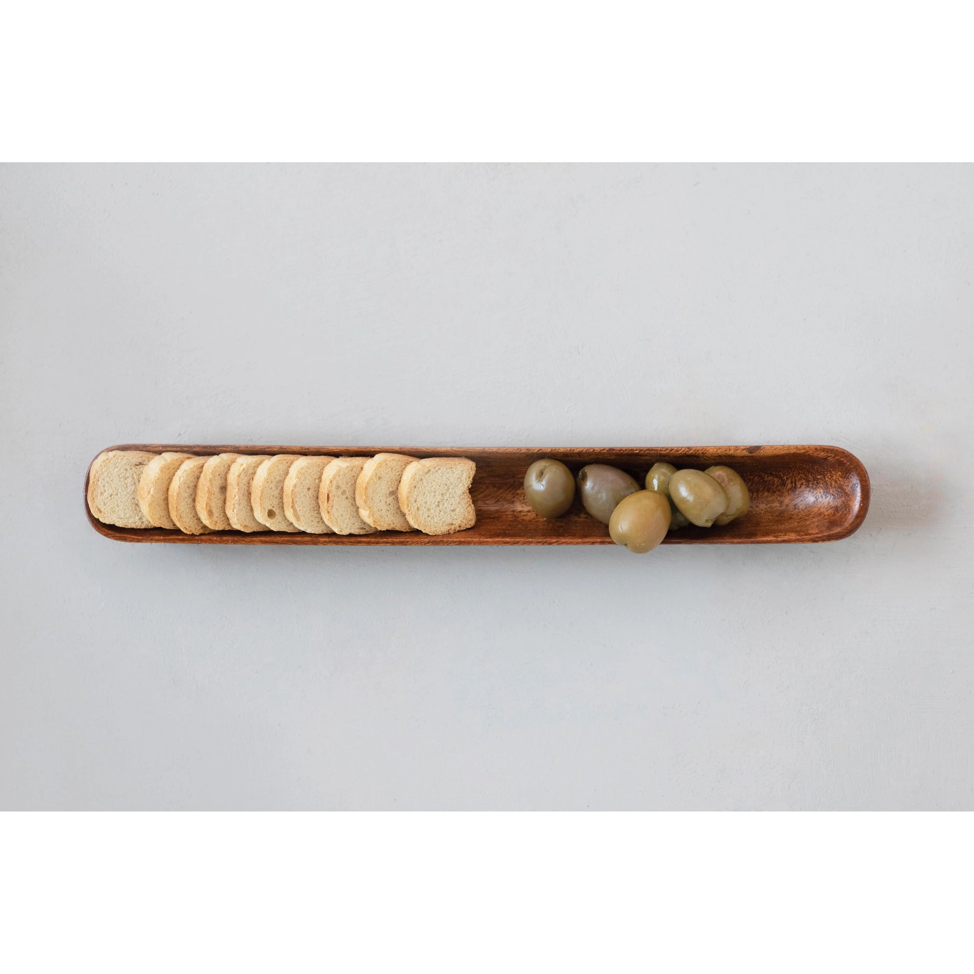 top view of the acacia wood olive boat displayed with crackers and green olives on a light gray background