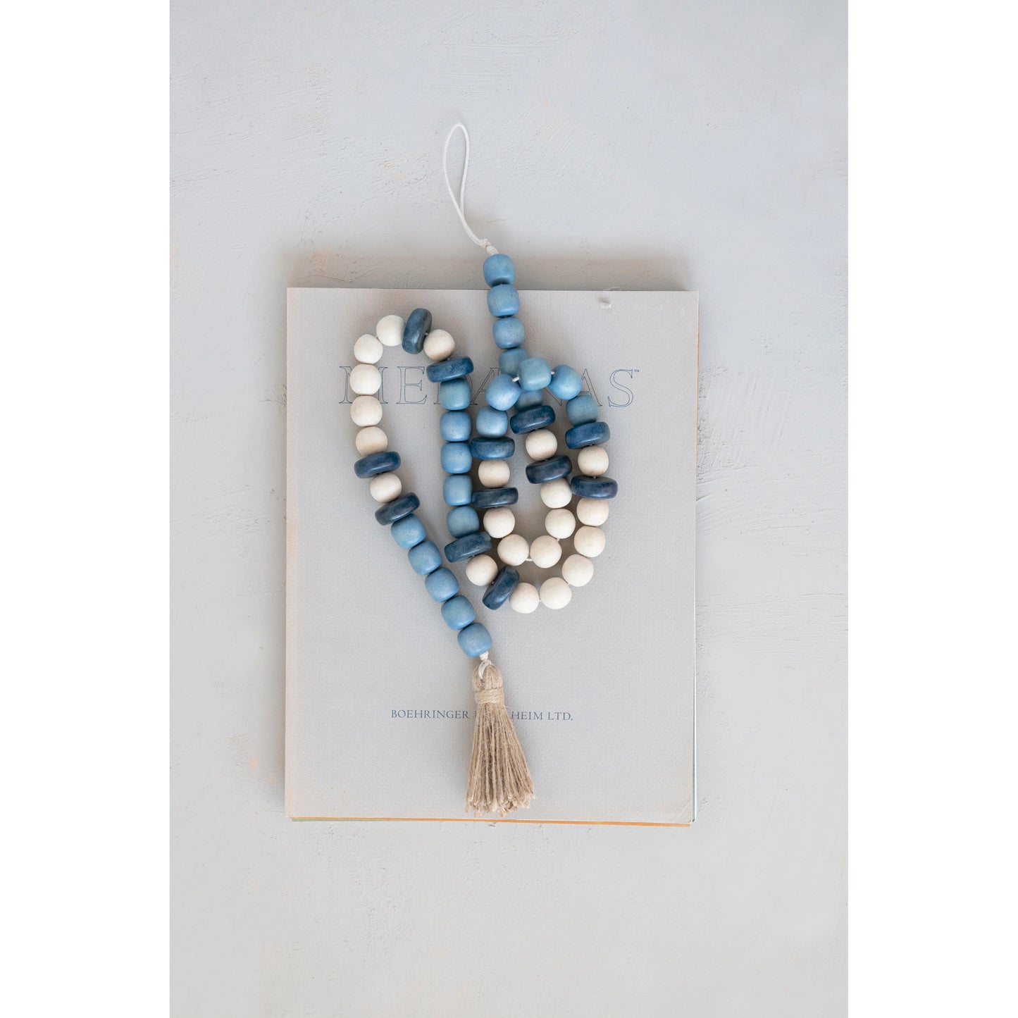blue and white beaded garland with a jute tassel on one end arranged on a book.