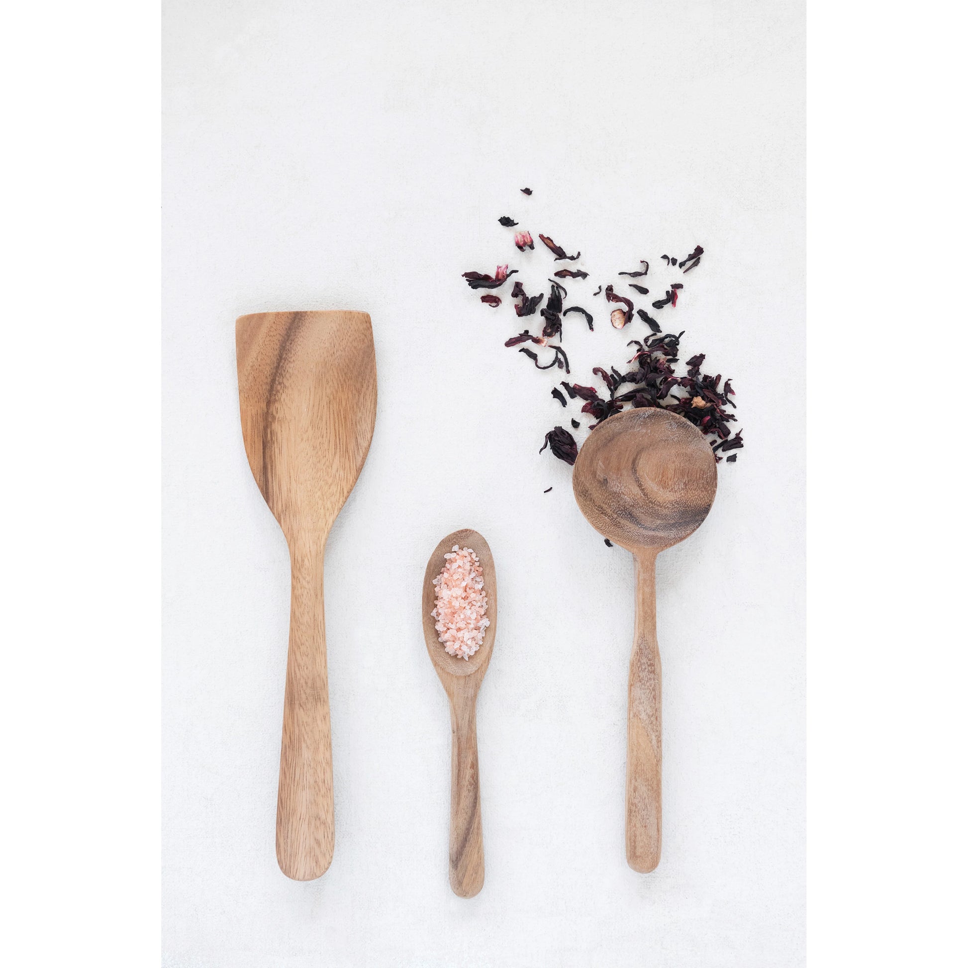 carved acacia wood spatula displayed next to two spoons and tea leaves on a white background