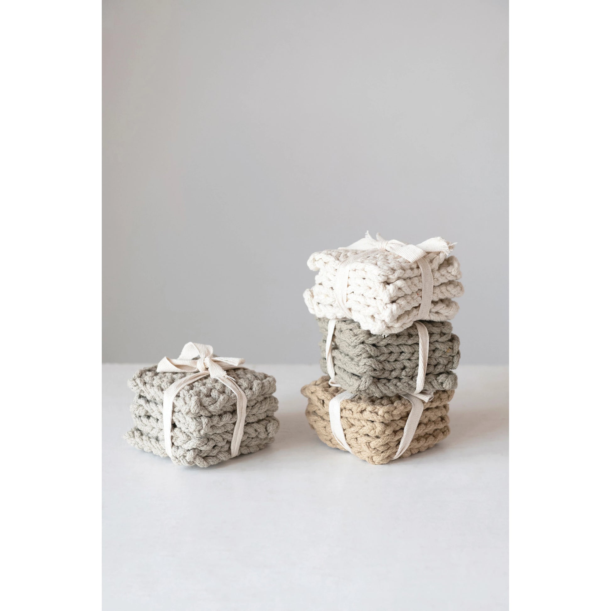 four different colored cotton crocheted coasters stacked on a white table against a light gray background