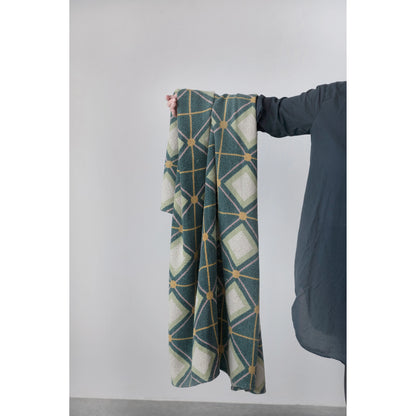 diamond pattern cotton throw displayed hanging over a womans arms against a gray background