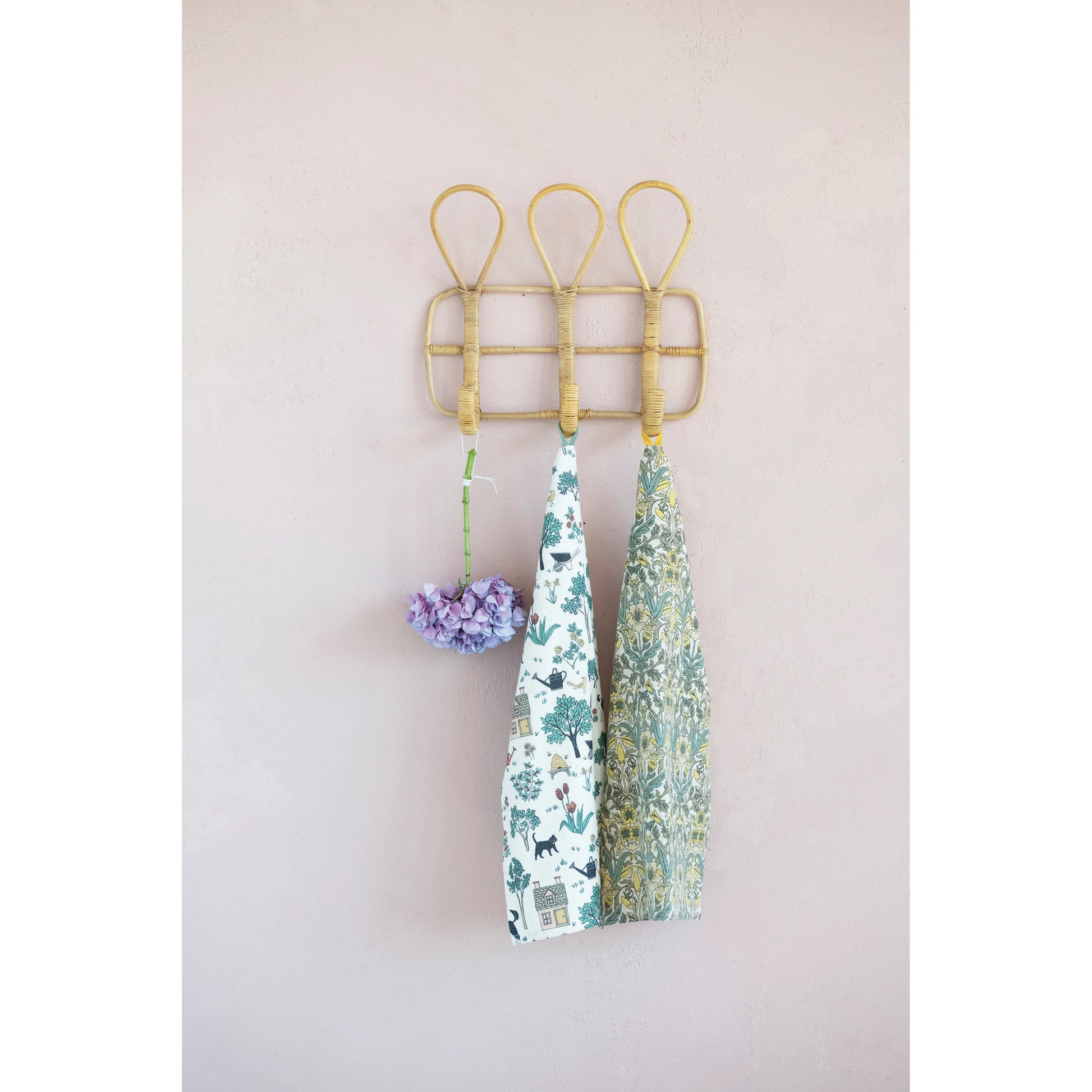 2 dish towels and a floral stem hanging on rattan wall hooks.