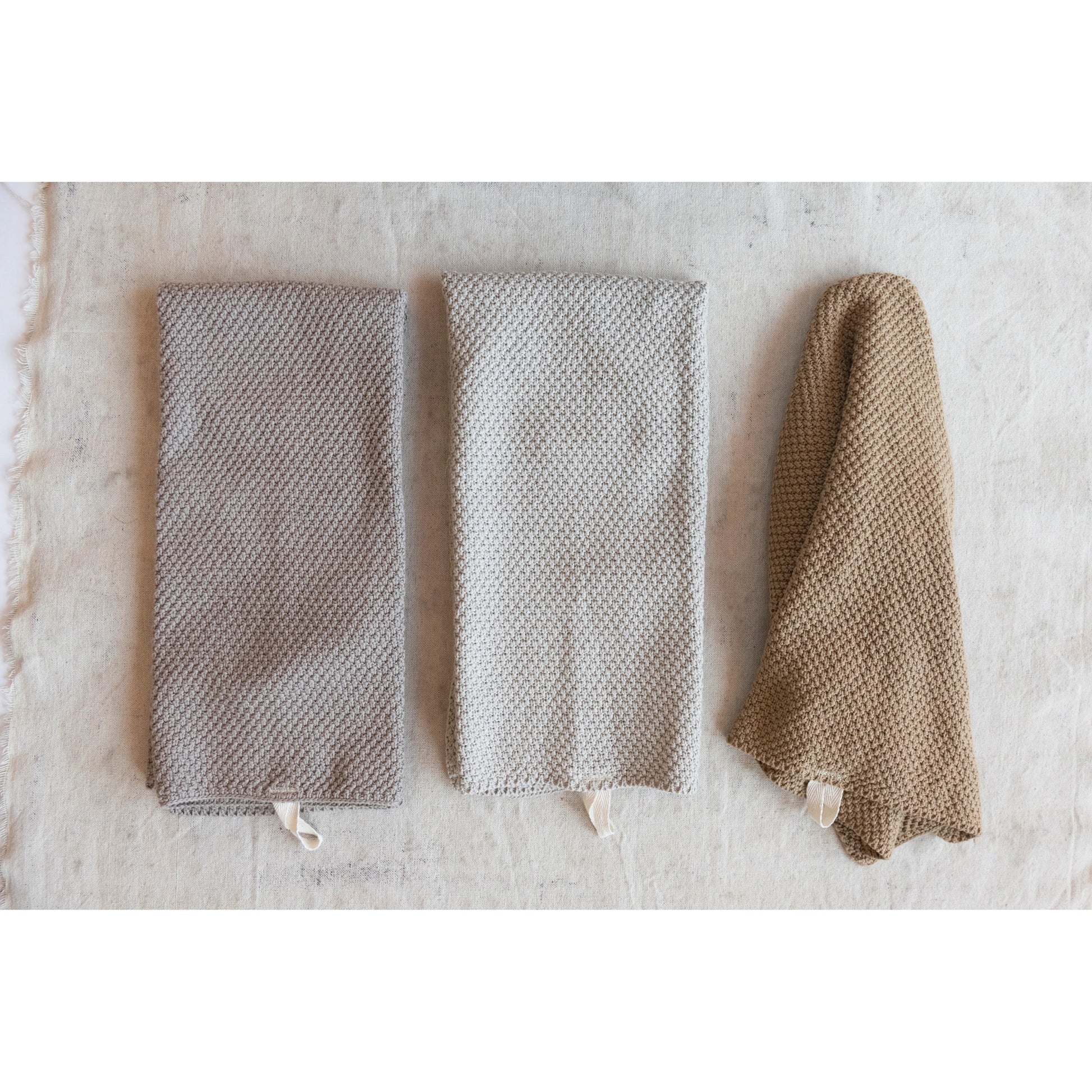 3 knit hand towels, 2 folded, 1 slightly unfolded, on a linen backdrop.