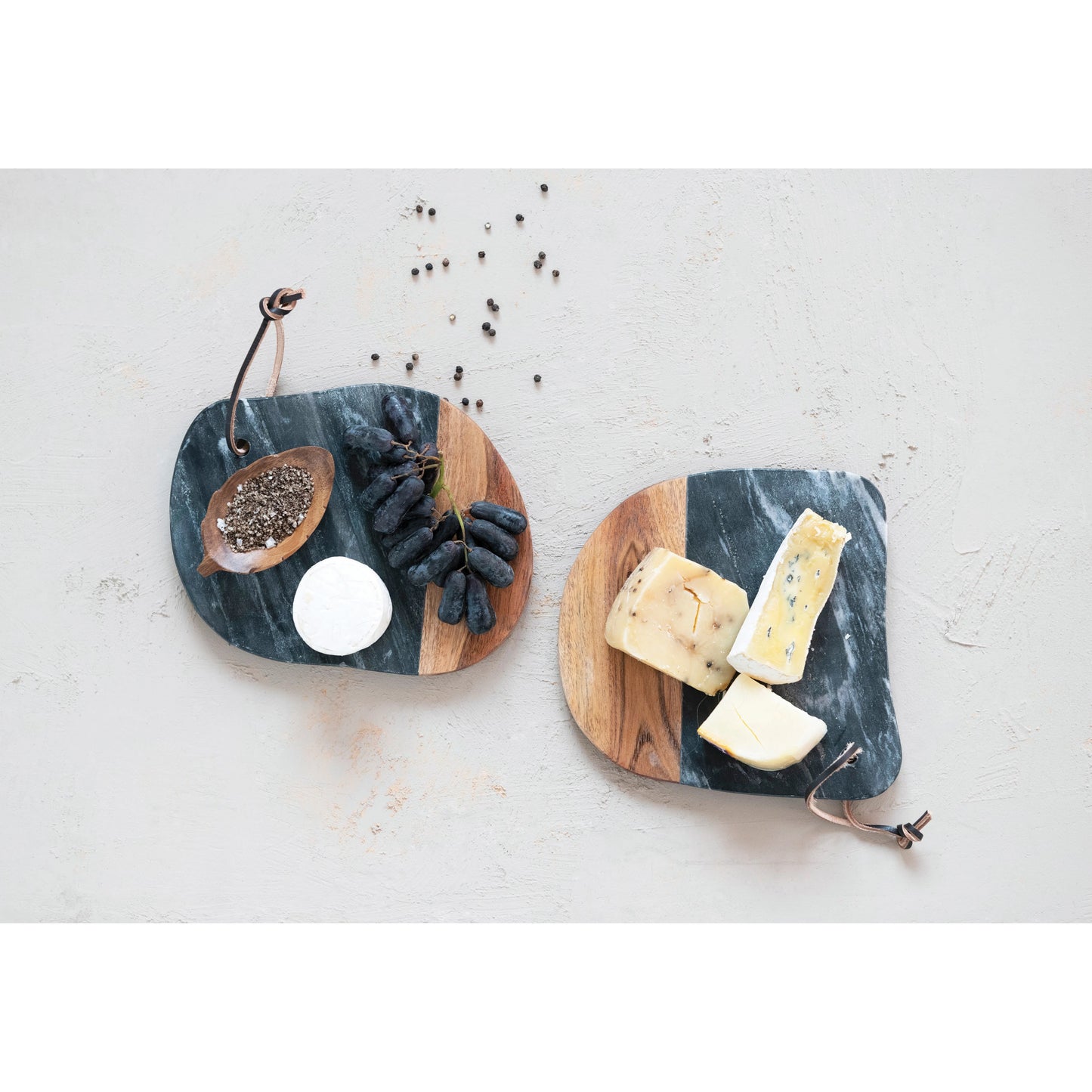 top view of two different styles of marble and acacia wood cheese boards displayed with fruit spices and cheese on a white surface
