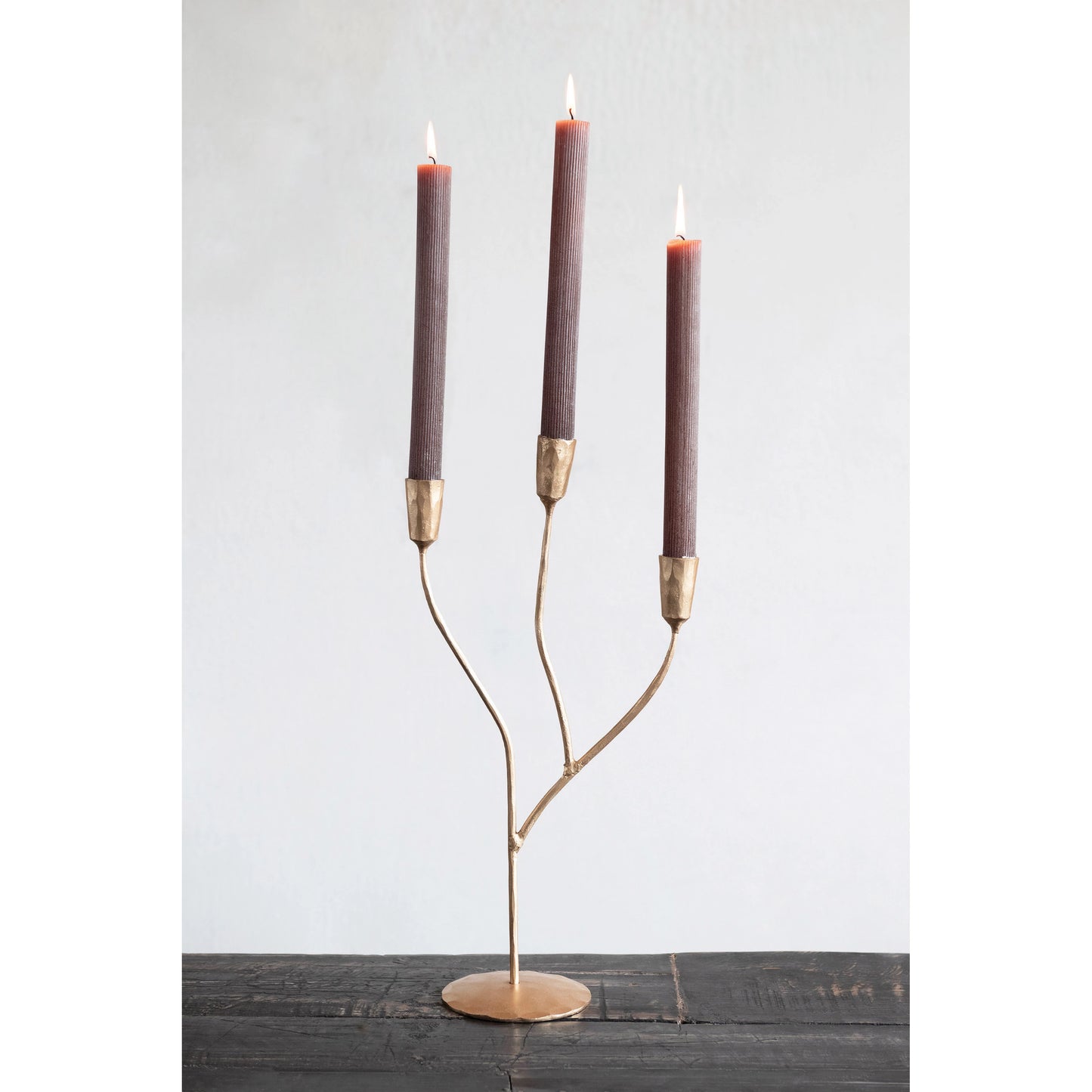 hand forged metal candelabra with candles displayed on a dark stained table against a white background