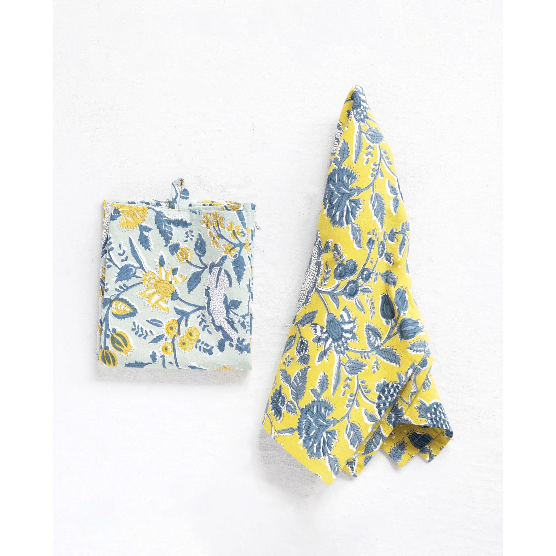 a folded blue and one yellow cotton tea towels with floral patterns hanging on a white background