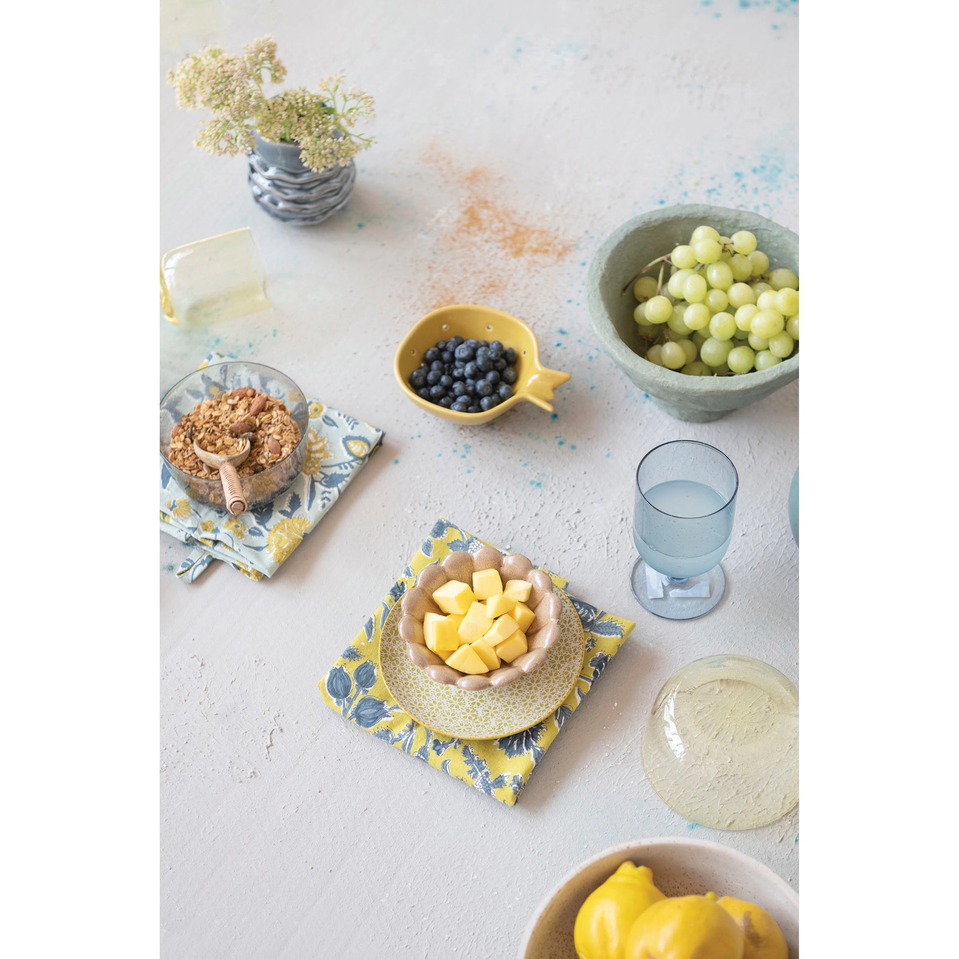 table display with the cottone tea towels with floral patterns drinking glass large bowl of grapes and small bowls with fruit on a white table