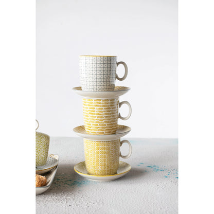 three different patterned stamped stoneware mugs stacked with saucers beside serving platters on a textured white surface