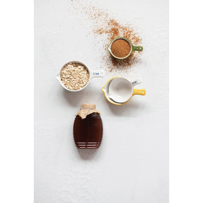 top view of the floral stoneware measuring cups displayed with seasonings and oats beside a jar of honey on a white background