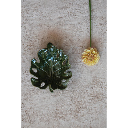 top view of leaf shaped bowl on a table with a flower set next to it.