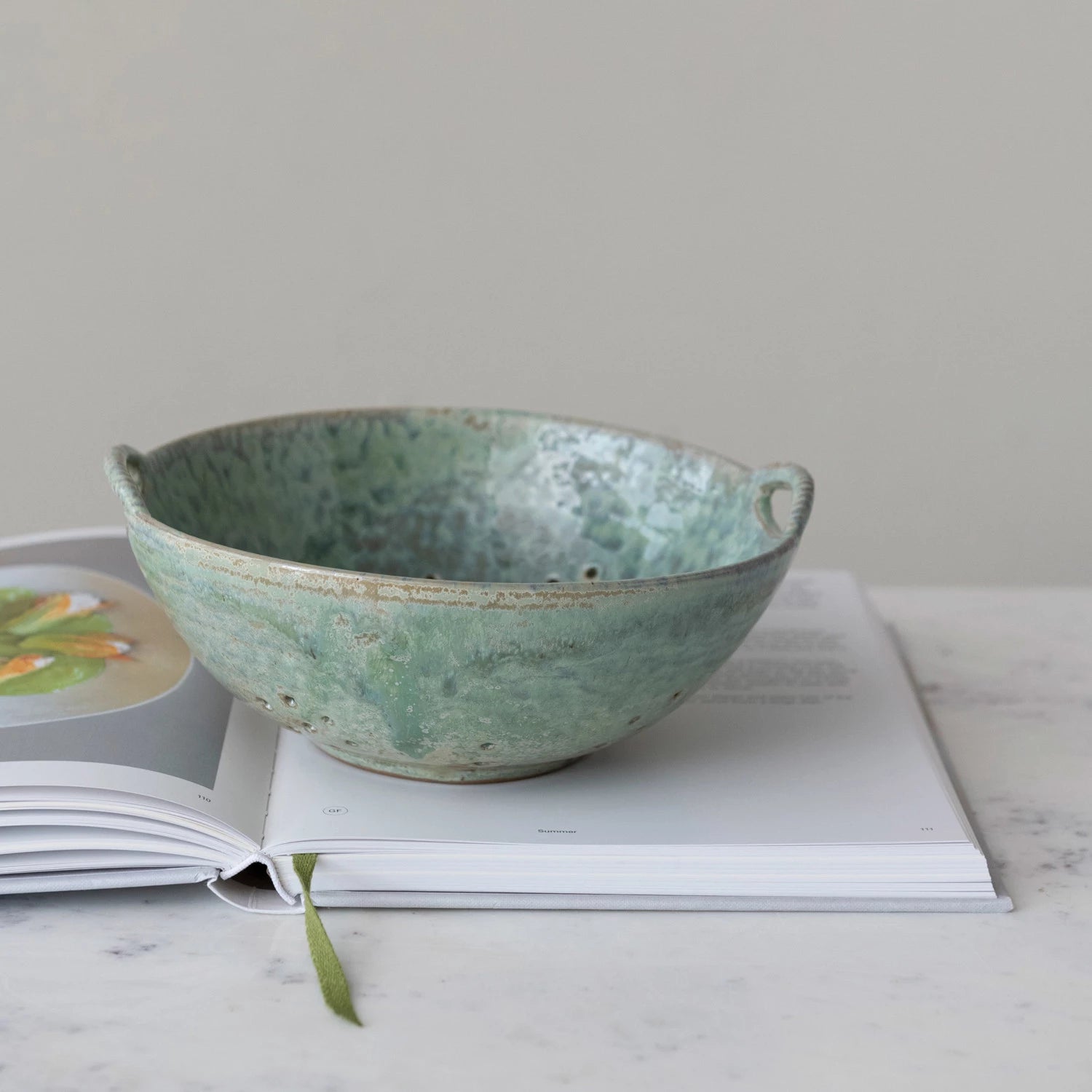 stoneware straining bowl with small side handle sitting on an open recipe book.