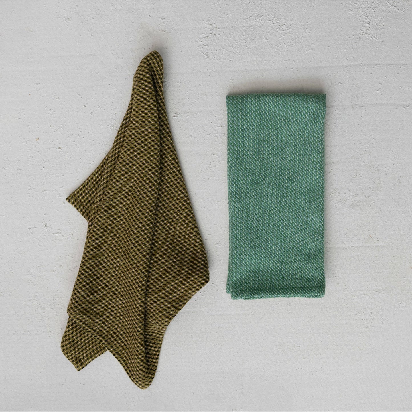 2 dishtowels, 1 olive green and laying in as if on a hook, the other, folded and blue green.