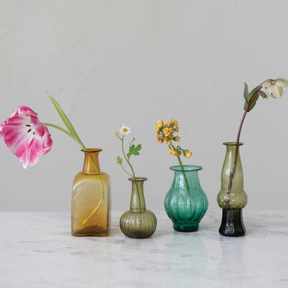 4 vases in assorted colors and shapes with a single flower stem in each on a countertop.