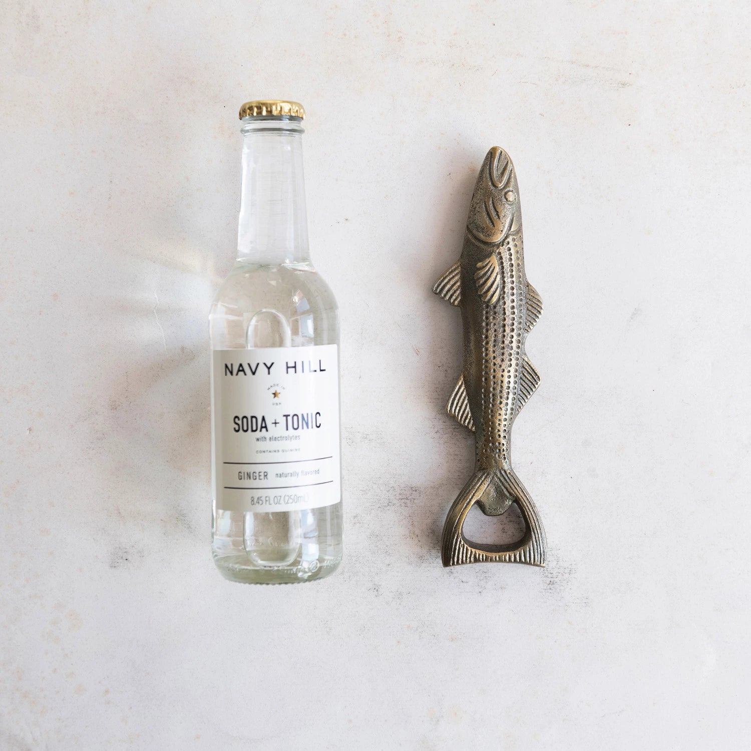 fish shaped bottle opener laying next to a bottle of soda and tonic.