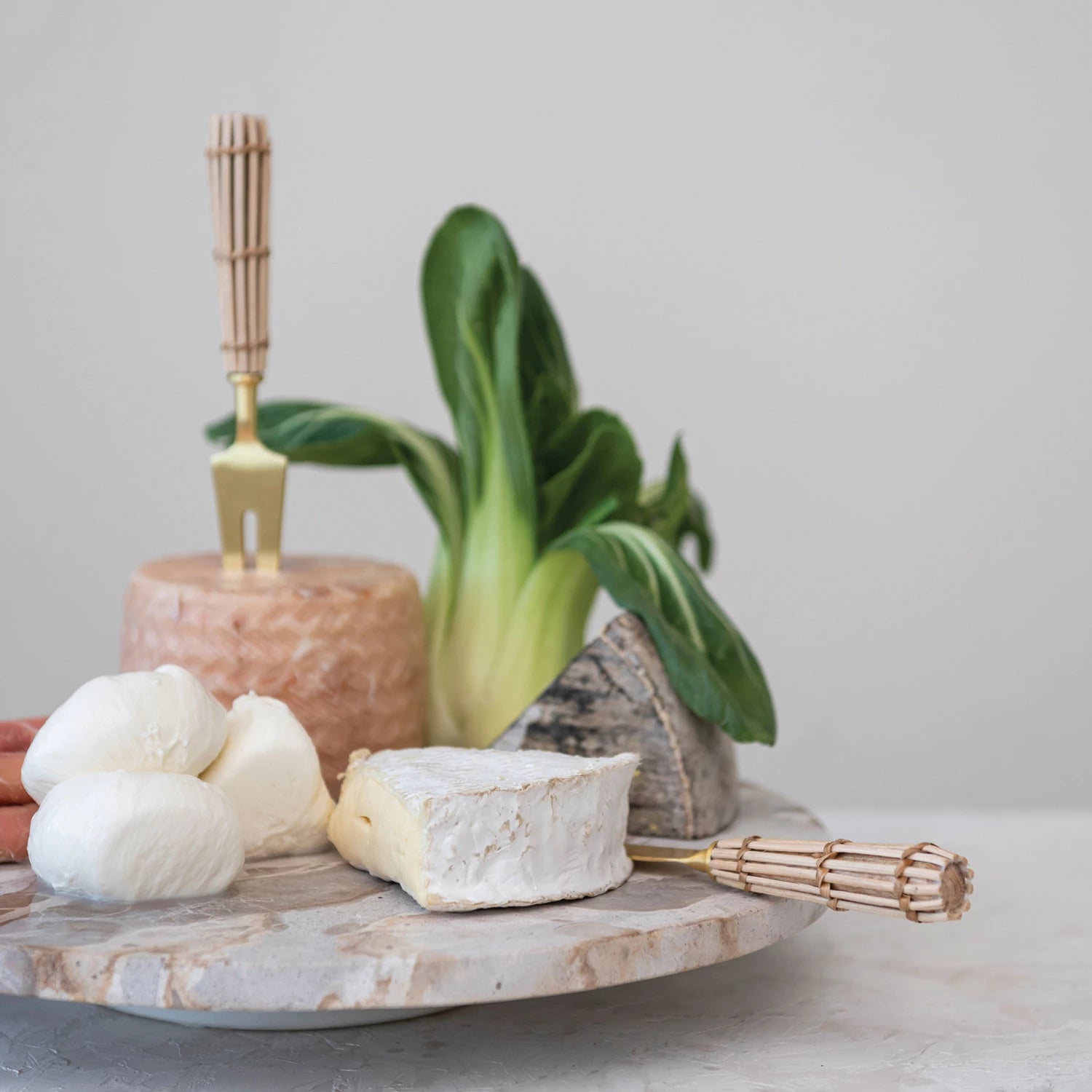 marble lazy susan with cheeses, Bok choi, and utensils on it.