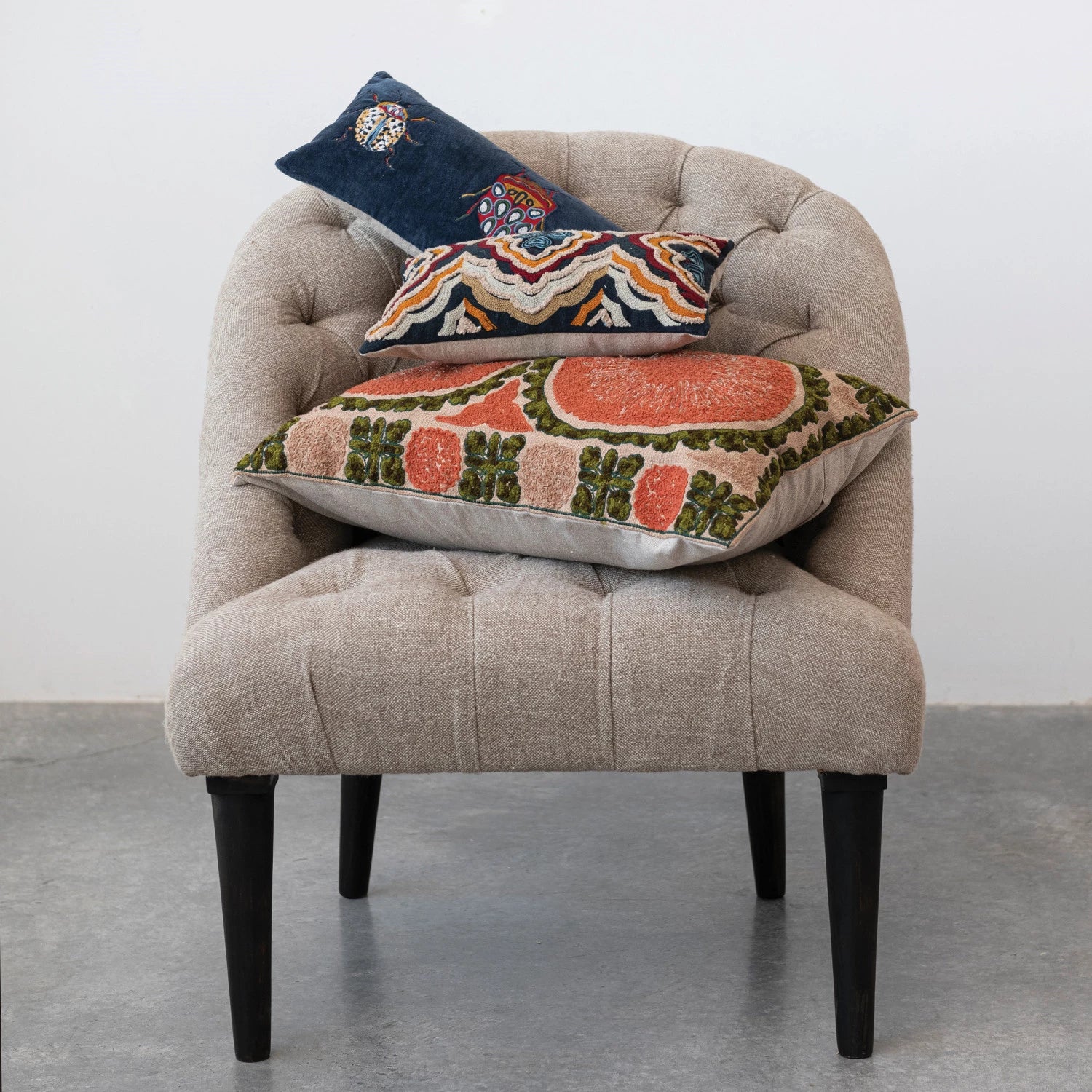 blue velvet embroidered lumbar pillow with beetles displayed at the top of a stack of pillows on a tan side chair