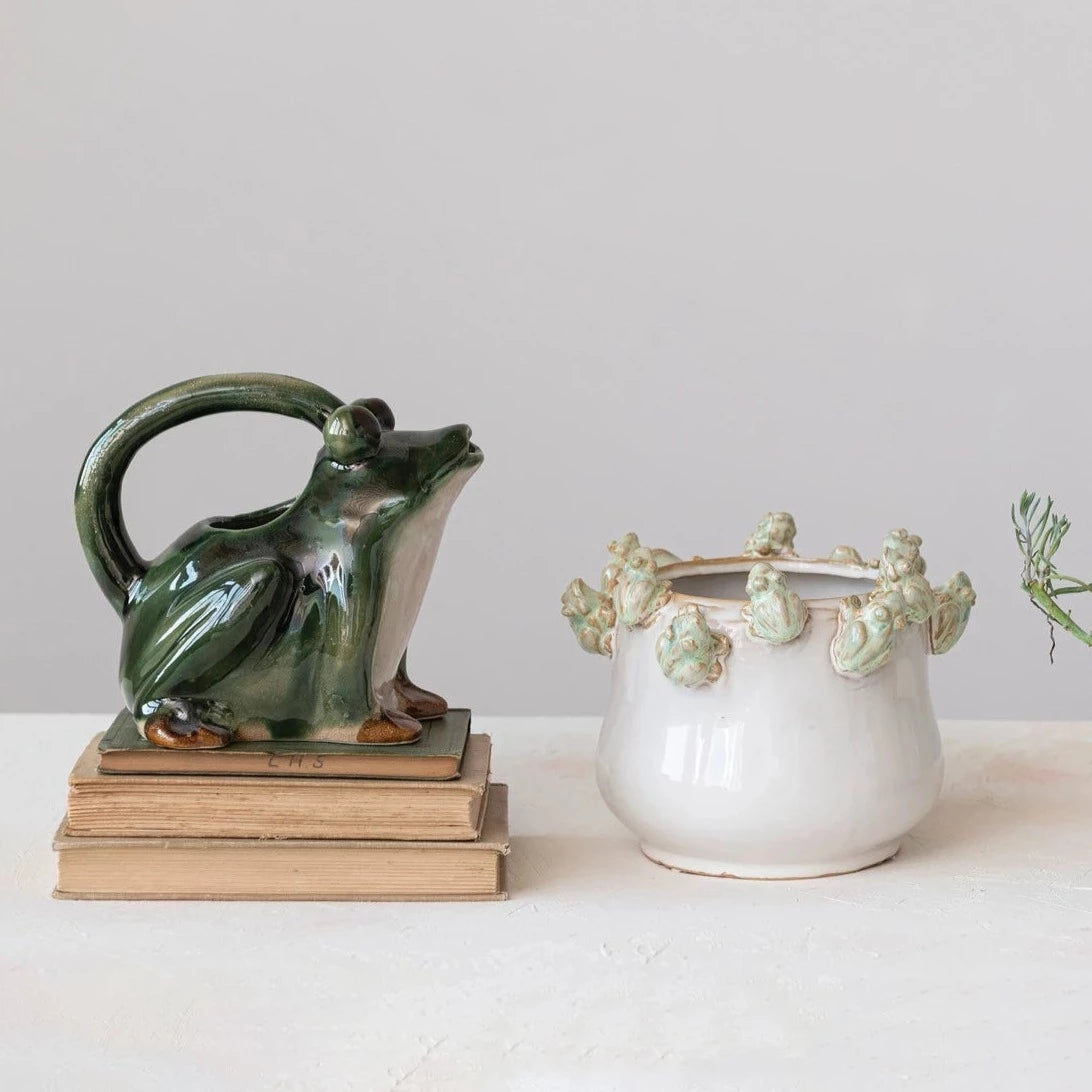 frog rimmed pot set on a table with a frog shaped watering pitcher next to it.