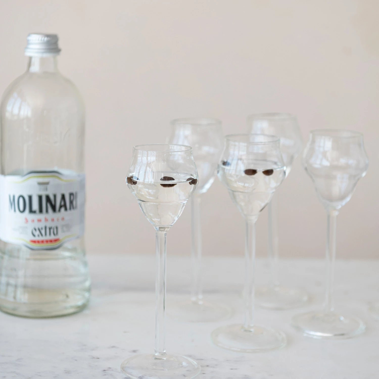 several stemmed sambuca glasses filled with drink and sitting next to a bottle