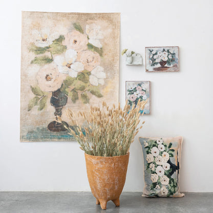 flowers and eyelash fringe lumbar pillow displayed leaning against a wall that has multiple floral pictures and next to a vase with dried grass
